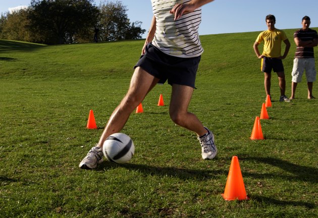 Men practising football, dribbling through cones in field