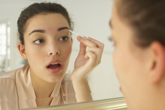 Young woman plucking eyebrows, close-up, reflection in mirror