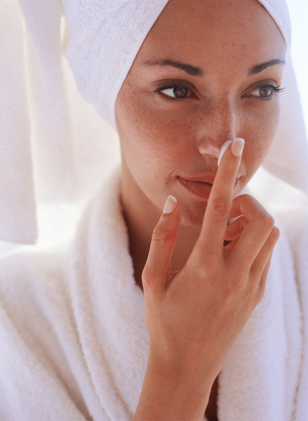 Woman in bathrobe putting lotin on nose