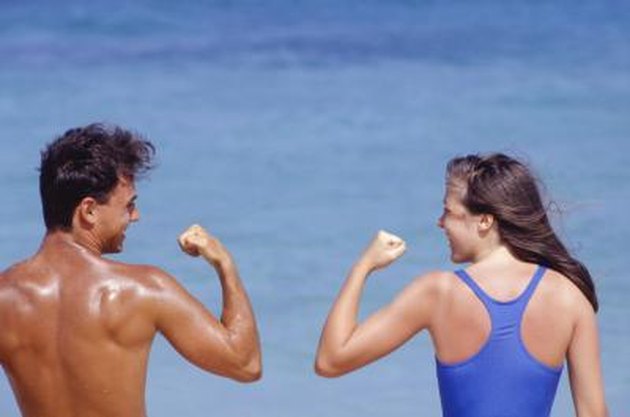 Couple flexing muscles by sea, rear view