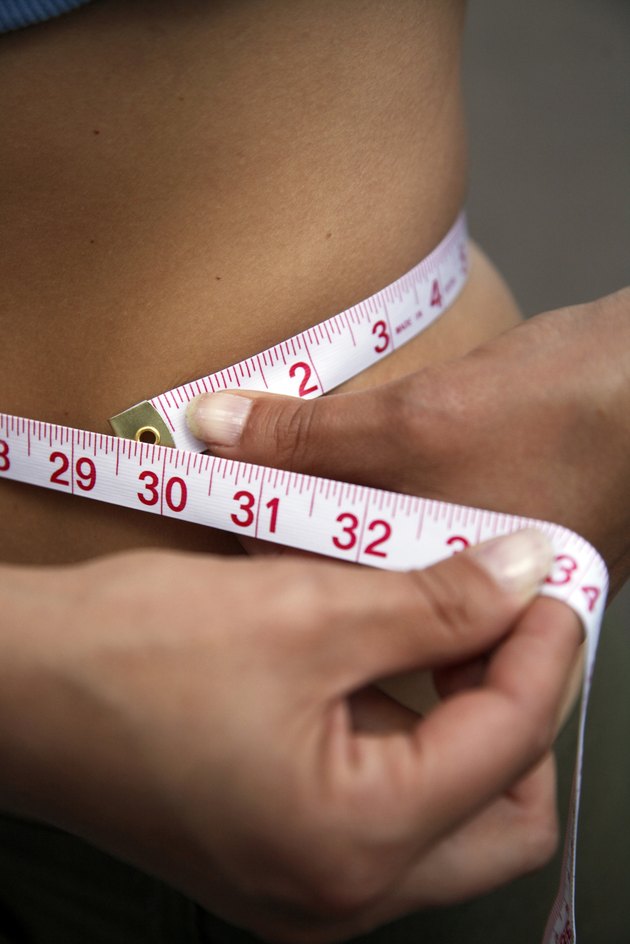 Mid section view of a woman measuring her waist with a tape measure