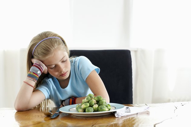 Girl (9-11) sitting at plate of sprouts