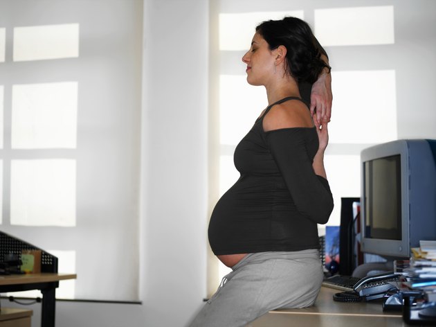 Pregnant young woman stretching by desk, profile