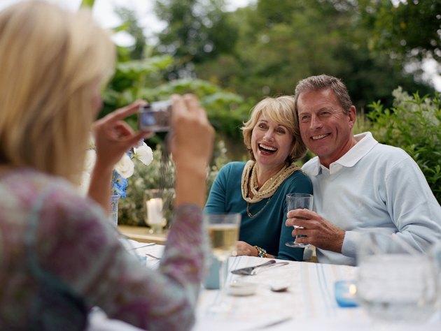 Woman taking photograph of couple at lunch table outdoors, smiling
