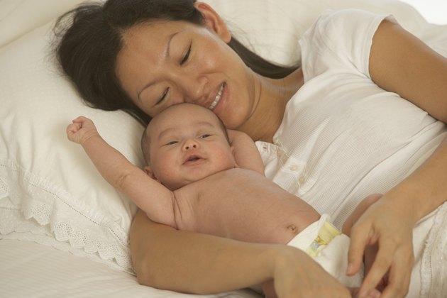 Asian mother laying in bed with newborn baby