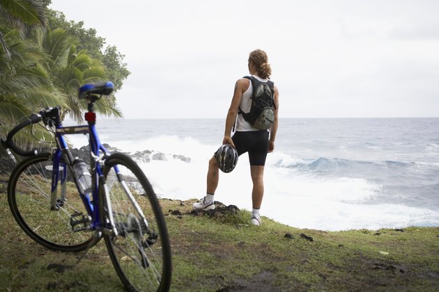 Male cyclist standing on cliff over ocean