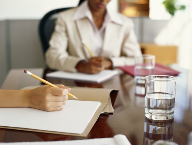 Businesspeople writing on conference table, focus on woman's hand in foreground