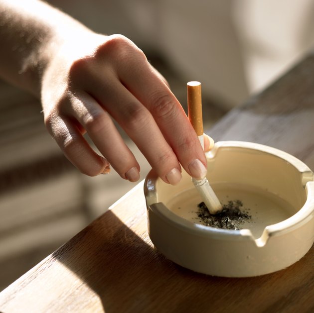 Hand holding cigarette in ashtray
