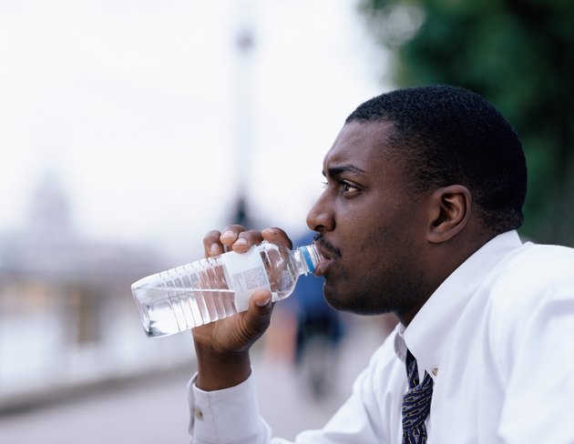 Side profile of a young man drinking water from a bottle outdoors
