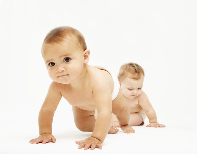 Female baby (6-9 months) crawling towards camera as another baby playing behind