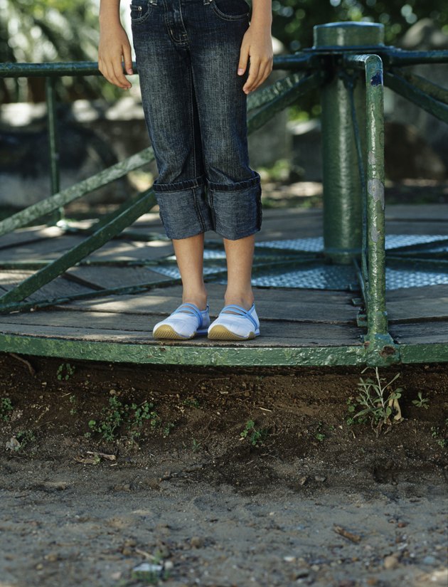 Girl (10-11) standing on roundabout in playground,low section