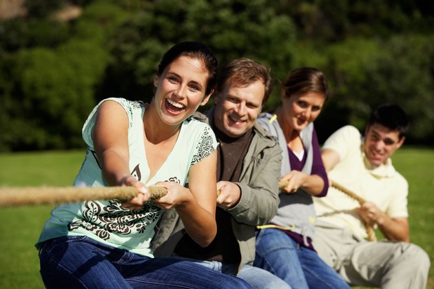 Friends playing tug-of-war in park (differential focus)