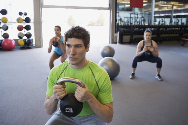 Serious exercise class doing kettlebell squats at gym