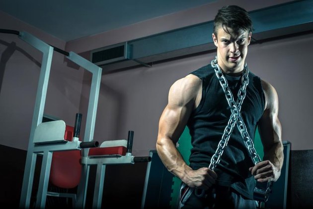 Young adult man posing in gym wearing iron chain around neck.