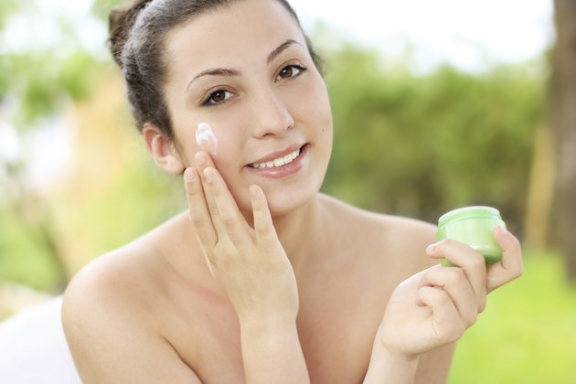 Portrait of young happy smiling beautiful woman applying creme