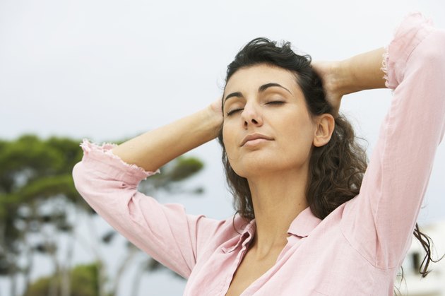Young woman with hands behind head, eyes closed, close-up, outdoors