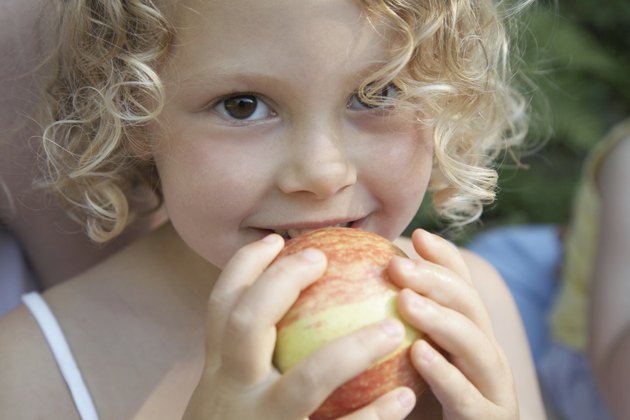 Girl (3-5) holding apple to mouth, smiling, portrait, close-up