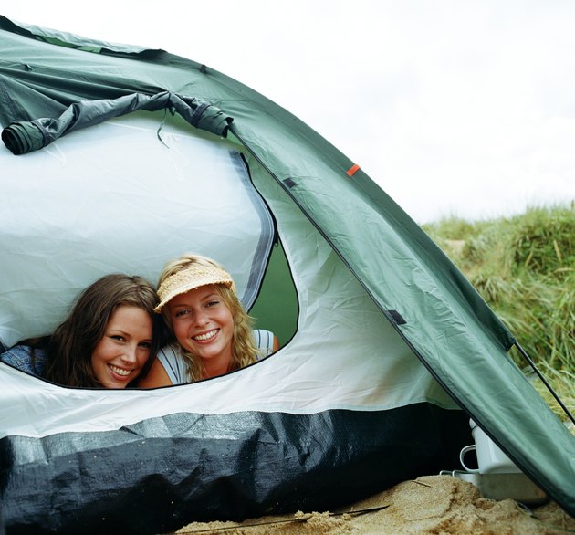 Two young women looking out tent opening, smiling, portrait