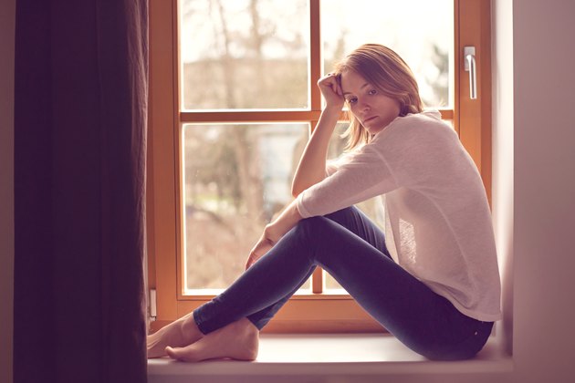 Young attractive woman, sitting on a window, looking outside