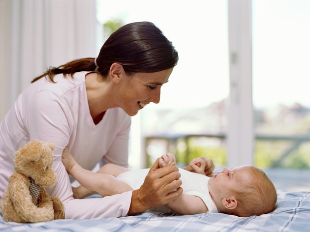 Mother holding baby girl's (6-9 months) legs, smiling