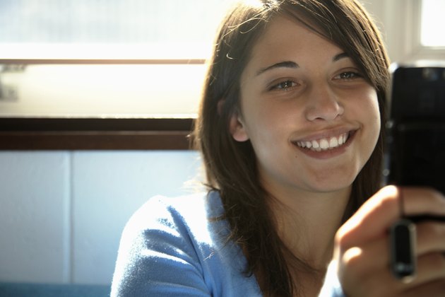 Teenage girl (15-17) using mobile phone, smiling (focus on girl)