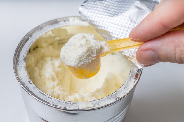 Hand holds scoop with newborn milk formula.