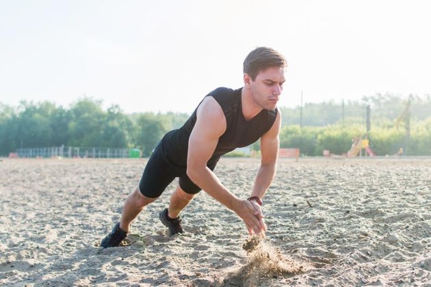 Fit man doing clapping push-ups during training exercise workout on beach in summer