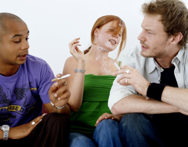 Young woman sitting between two young men smoking cigarettes