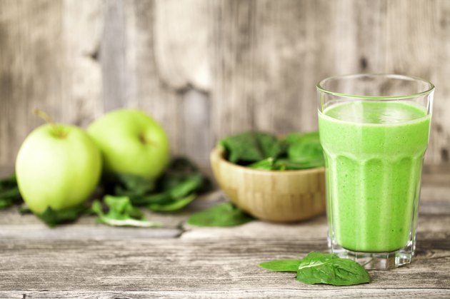 green smoothie juice on wooden table with spinach and apples