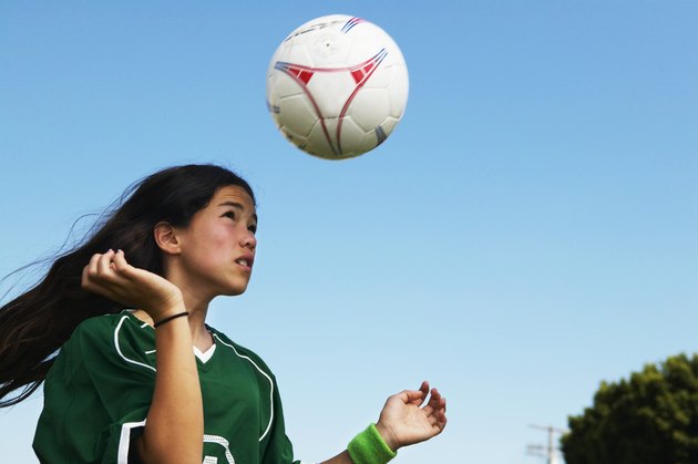 Female footballer (11-13) heading ball, low angle view