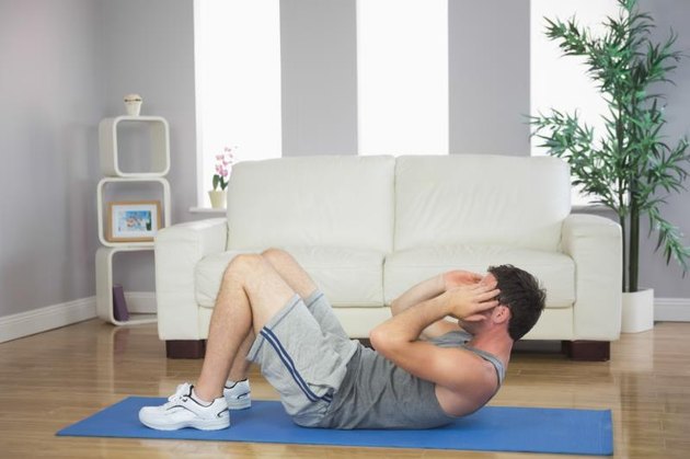 Handsome sporty man doing sit ups in bright living room