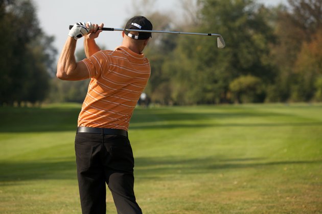"Young man swinging golf club, rear view"