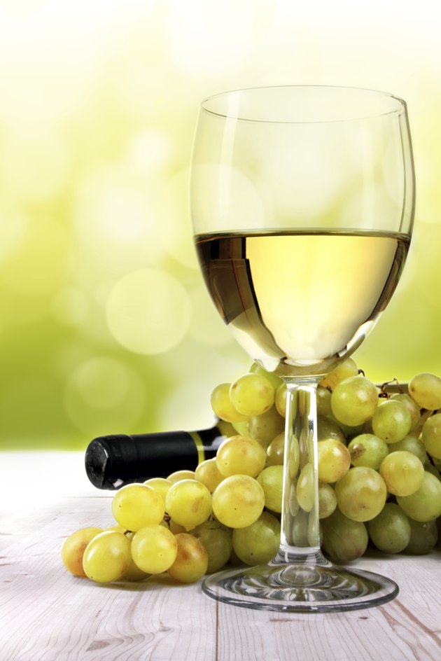 White wine glass, grapes and bottle on table in vineyard