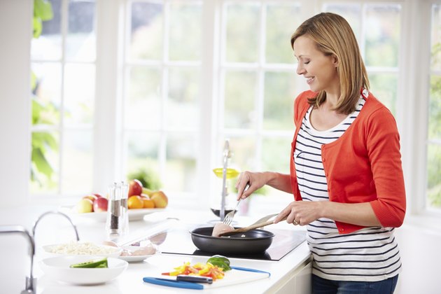 Woman Standing At Hob Preparing Meal In Kitchen