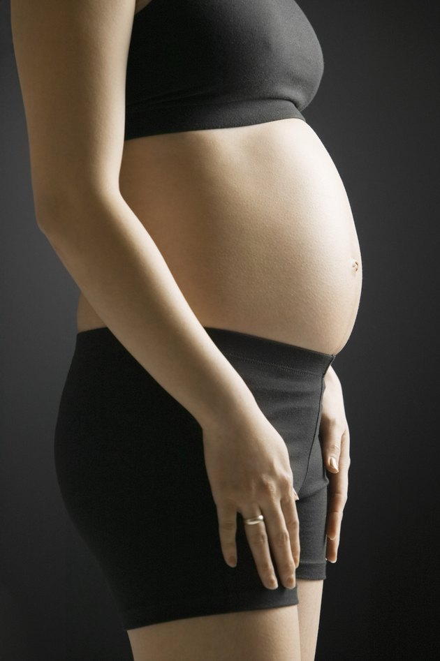 Pregnant young woman standing in studio, mid section