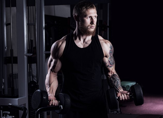 athletic guy bodybuilder , execute exercise with dumbbells, in dark gym