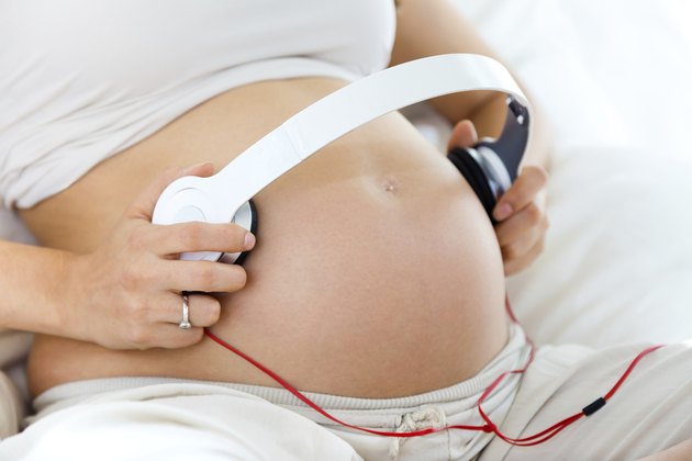 Pregnant woman putting headphones on her belly
