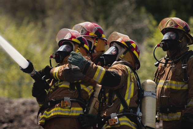 a group of firefighters in full gear dowse a fire with a firehose