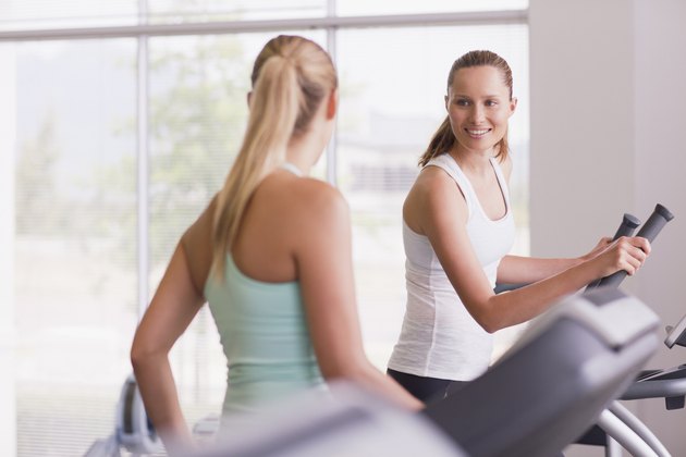 Smiling women using exercise equipment in gymnasium