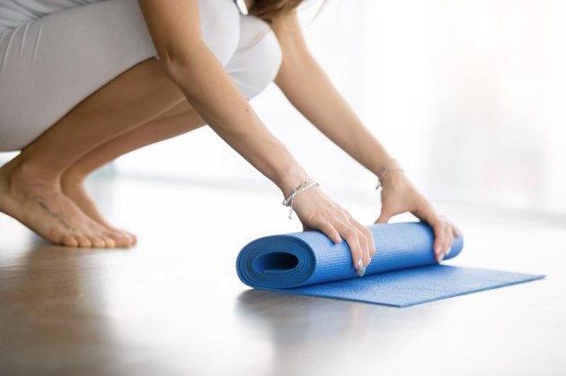 Close up shot of female hands unrolling yoga mat in a modern apartment, preparing for practice in class or at home. Yoga studio etiquette. Healthy lifestyle concept