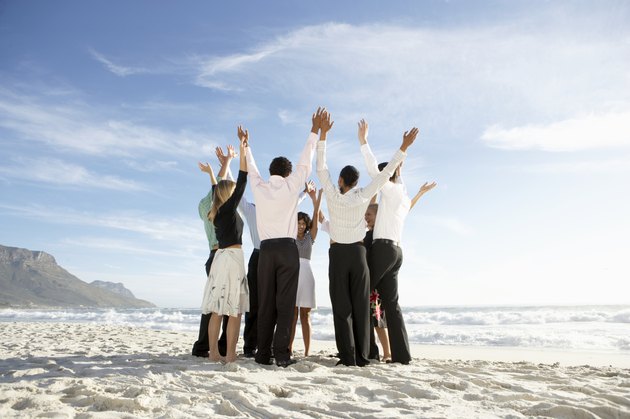 Group of people standing in circle on beach, arms raised