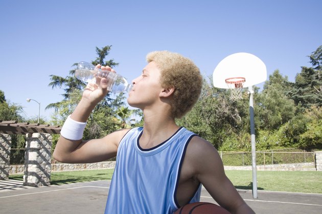 Teenage boy on basketball court drinking water bottle