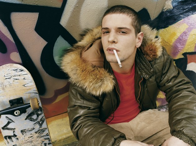 Teenage Boy Crouching in an Alley Smoking a Cigarette