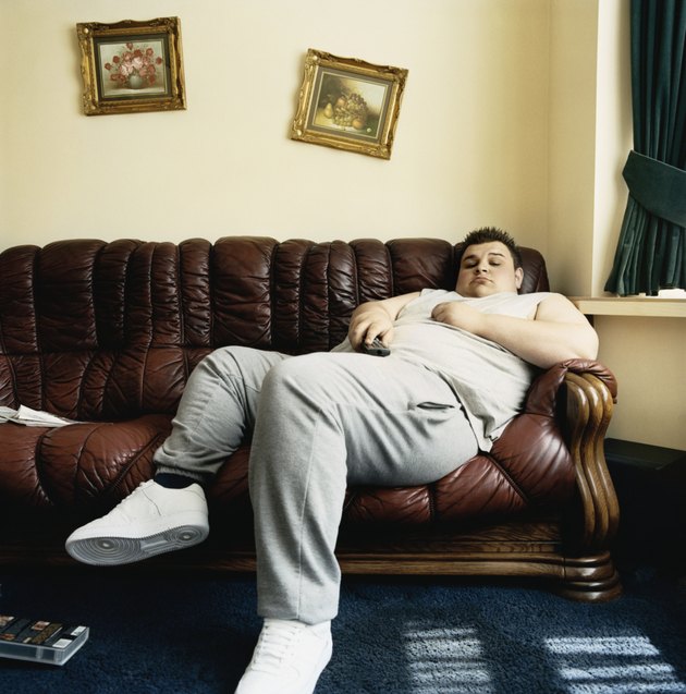 Overweight Young Man Falls Asleep While Lying on a Sofa Watching TV