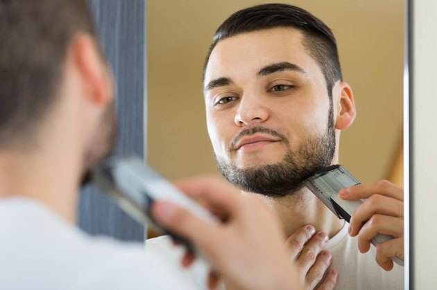 Man looking at mirror and shaving beard with trimmer
