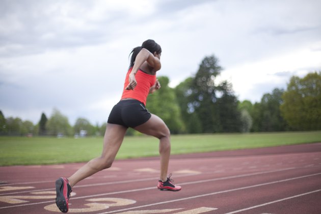 Young female sprinter accelerating, running, rear view
