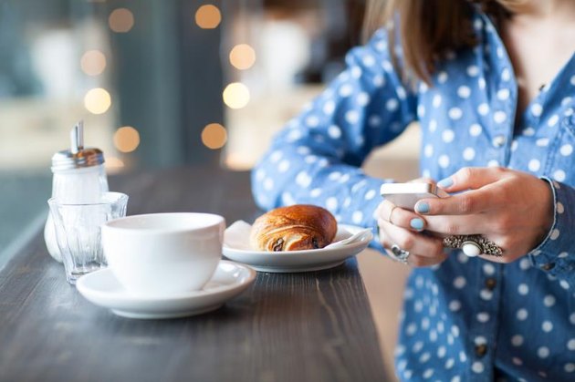 Midsection of woman using mobile phone with coffee and snack at cafe counter