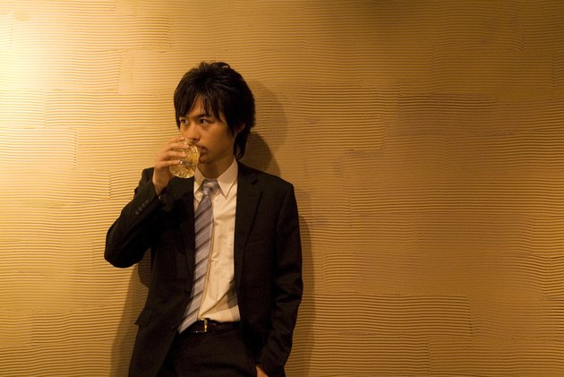 Businessman leaning against a wall with a drink