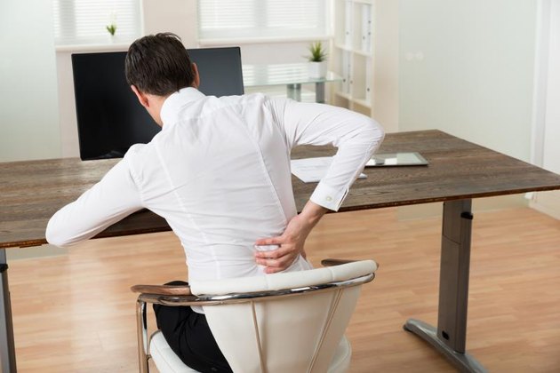 Young Businessman Sitting On Chair And Suffering From Backache At Desk