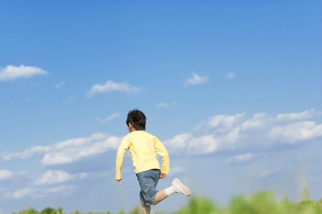 Rear view of young boy running against a blue sky